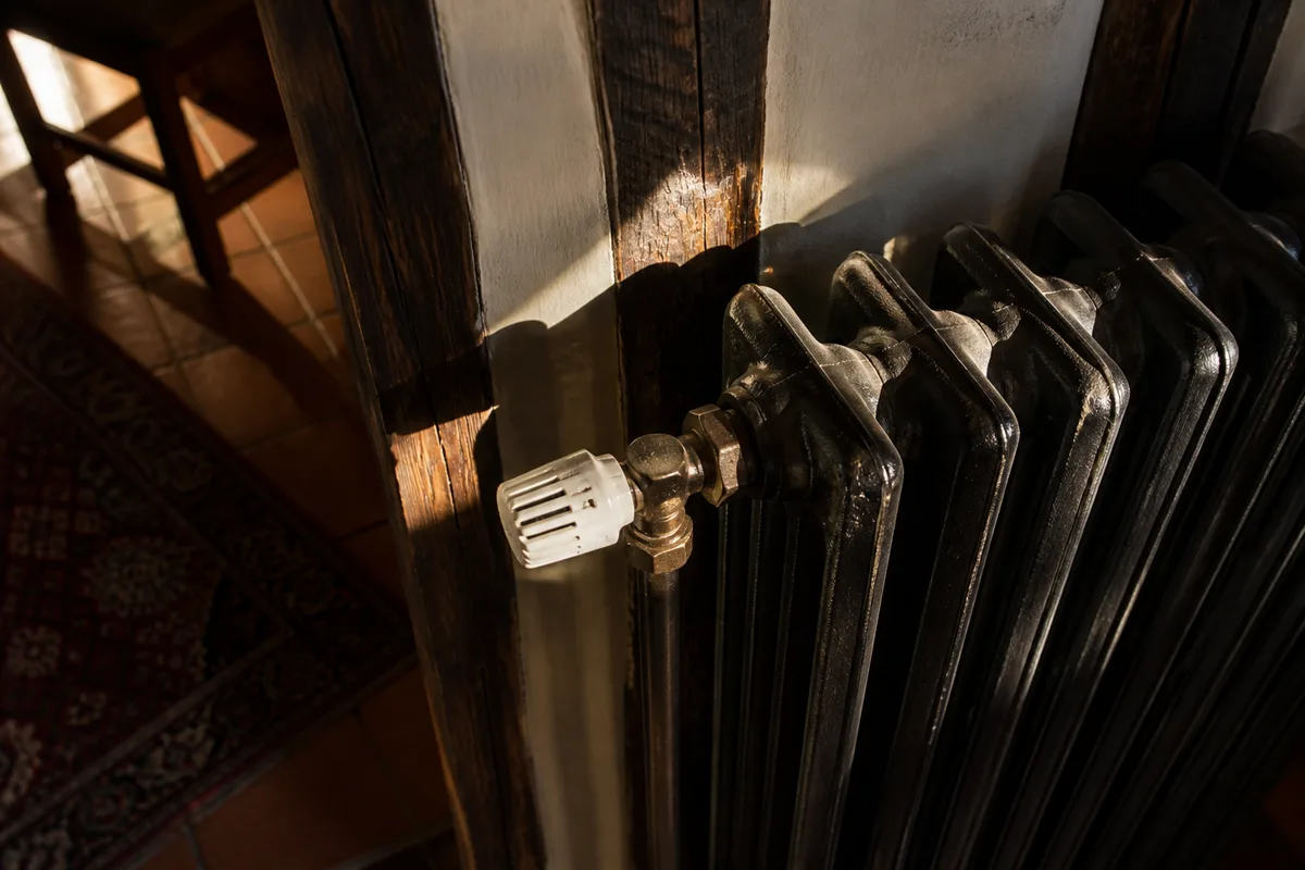 Radiateur ancien en fonte dans une pièce de maison normande, robinet thermostatique en gros plan